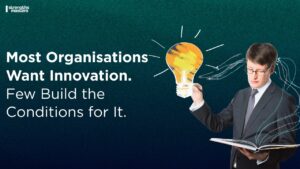 Business professional holding an open book with a glowing lightbulb illustration above it, alongside text reading “Most Organisations Want Innovation. Few Build the Conditions for It.” and Strengths Masters logo.